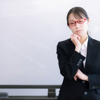 困惑する赤い眼鏡の女性指導員がホワイトボードの前で考えるの写真