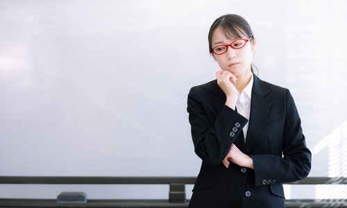 困惑する赤い眼鏡の女性指導員がホワイトボードの前で考える