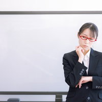 セミナーで困惑し首をかしげる赤いスーツの女性講師の写真