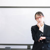 疑問に思う赤い眼鏡をかけた女性講師がセミナーで考える様子の写真