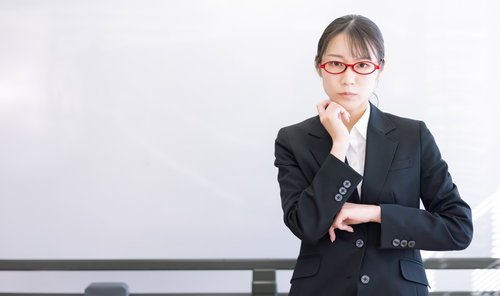 ホワイトボードの前で真剣な眼差しの赤い眼鏡をかけた女性講師