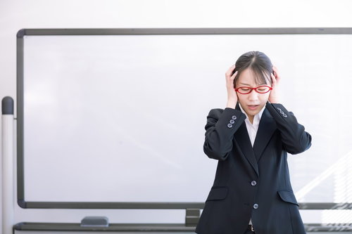 ホワイトボード前で頭を抱える赤い眼鏡の女性講師