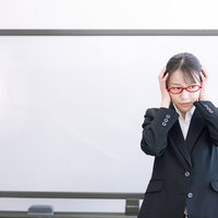 セミナー中に後悔して頭を抱える赤い眼鏡の女性講師の写真