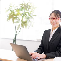 笑顔でコンサルするスーツ姿の女性秘書とノートパソコンの写真
