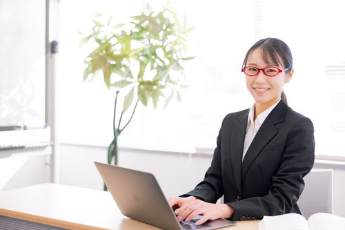 笑顔でコンサルするスーツ姿の女性秘書とノートパソコン