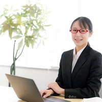 白いデスクで笑顔の受付対応をする黒いスーツの女性の写真