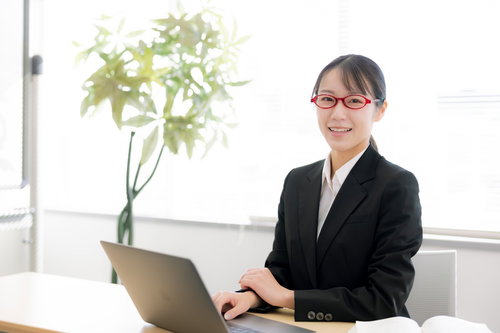 白いデスクで笑顔の受付対応をする黒いスーツの女性