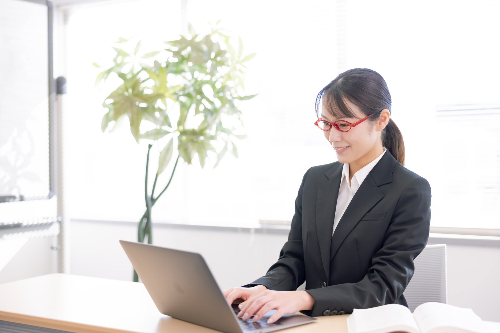 デスクでノートパソコンを操作するスーツ姿の女性［モデル：SAKI］
