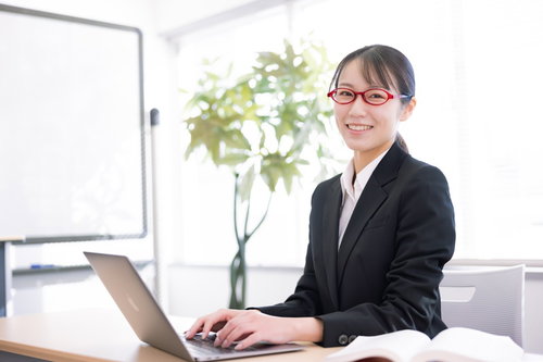 黒いスーツ姿の笑顔の受付嬢がノートパソコンで対応