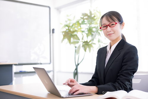 黒いスーツで笑顔の受付をする女性従業員がノートパソコンで対応