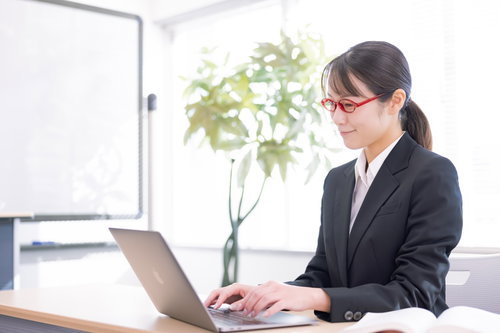 デスクワークしながらランチに何を食べようか考える黒いスーツの女性社員