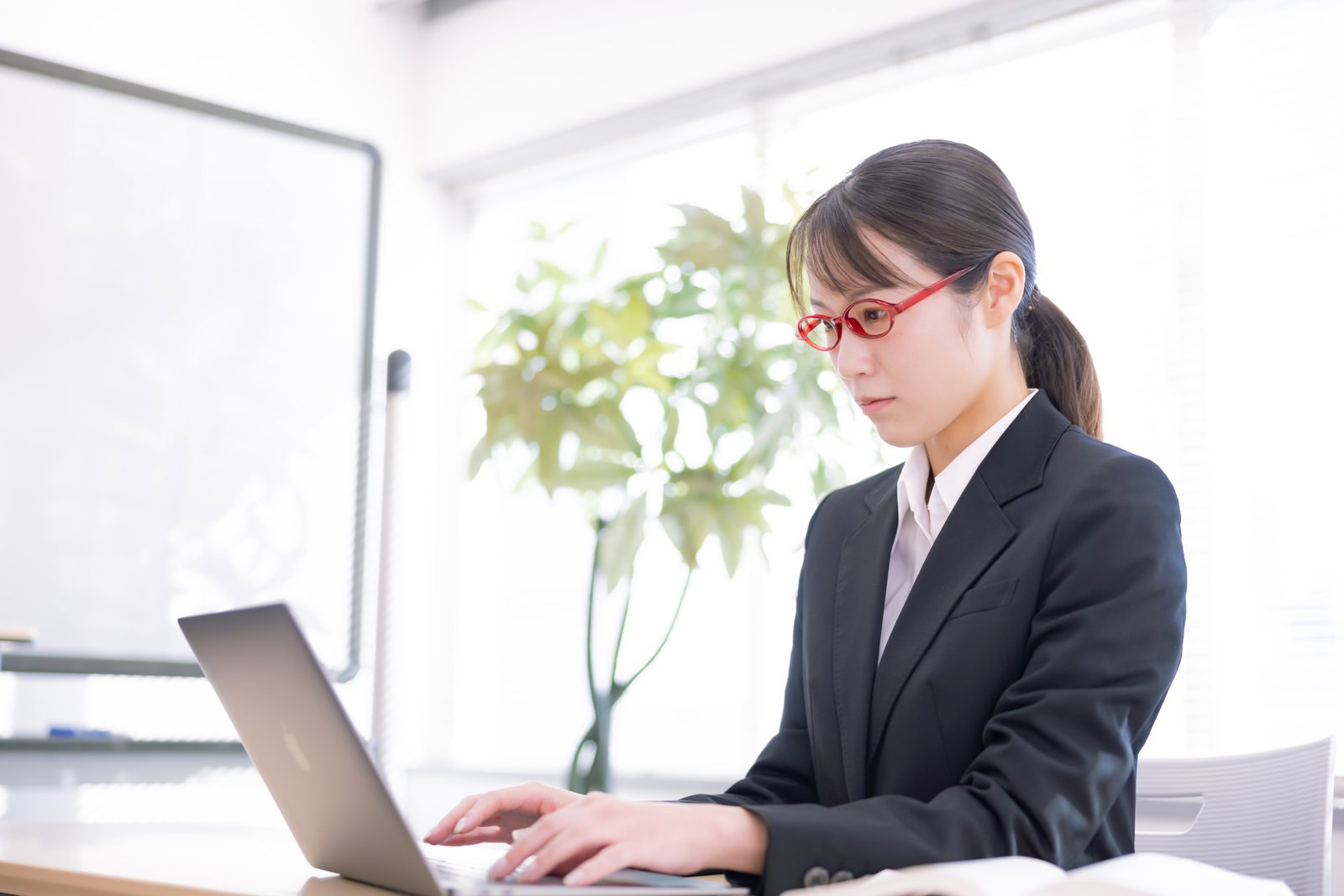黒いスーツを着た女性がパソコンに向かって真剣に作業している様子［モデル：SAKI］