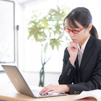 ノートパソコンの前で首をかしげる受付の女性の写真