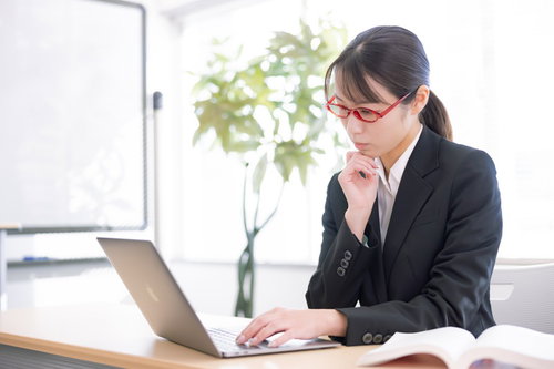ノートパソコンの前で首をかしげる受付の女性
