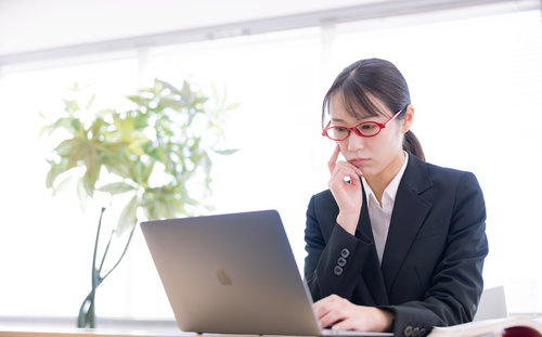 ノートパソコンの画面を見つめて考え込むスーツ姿の女性