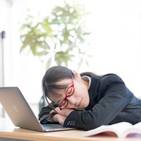 研修の合間にノートパソコンの前で居眠りする女性の写真