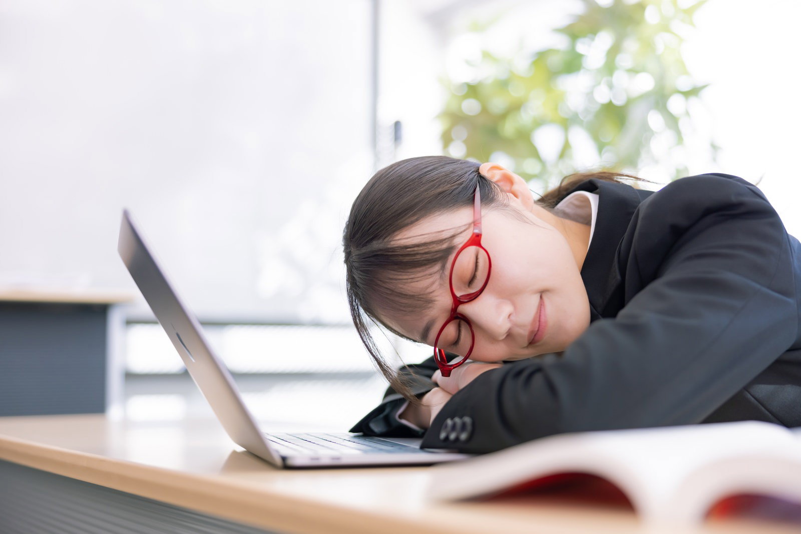 ノートパソコンの前で腕を枕にして居眠りする眼鏡をかけた女性［モデル：SAKI］