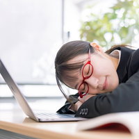 デスクで昼寝する眼鏡をかけた女性社員、ノートパソコンの前で休憩の写真