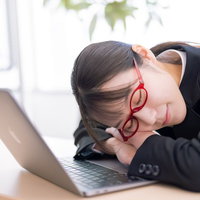 休憩中にノートパソコンの前で昼寝する女性社員の写真