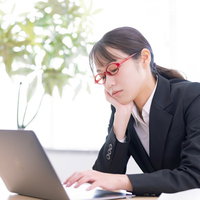 肘をついてうとうとしながらデスクワークをする女性の写真