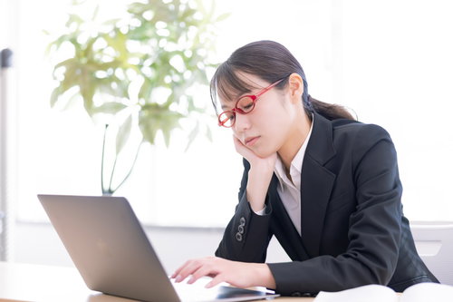 肘をついてうとうとしながらデスクワークをする女性