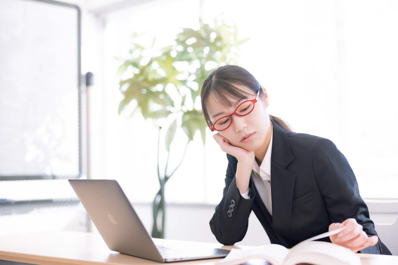 肘をついてパソコンで調べものをしている事務員の女性［モデル：SAKI］