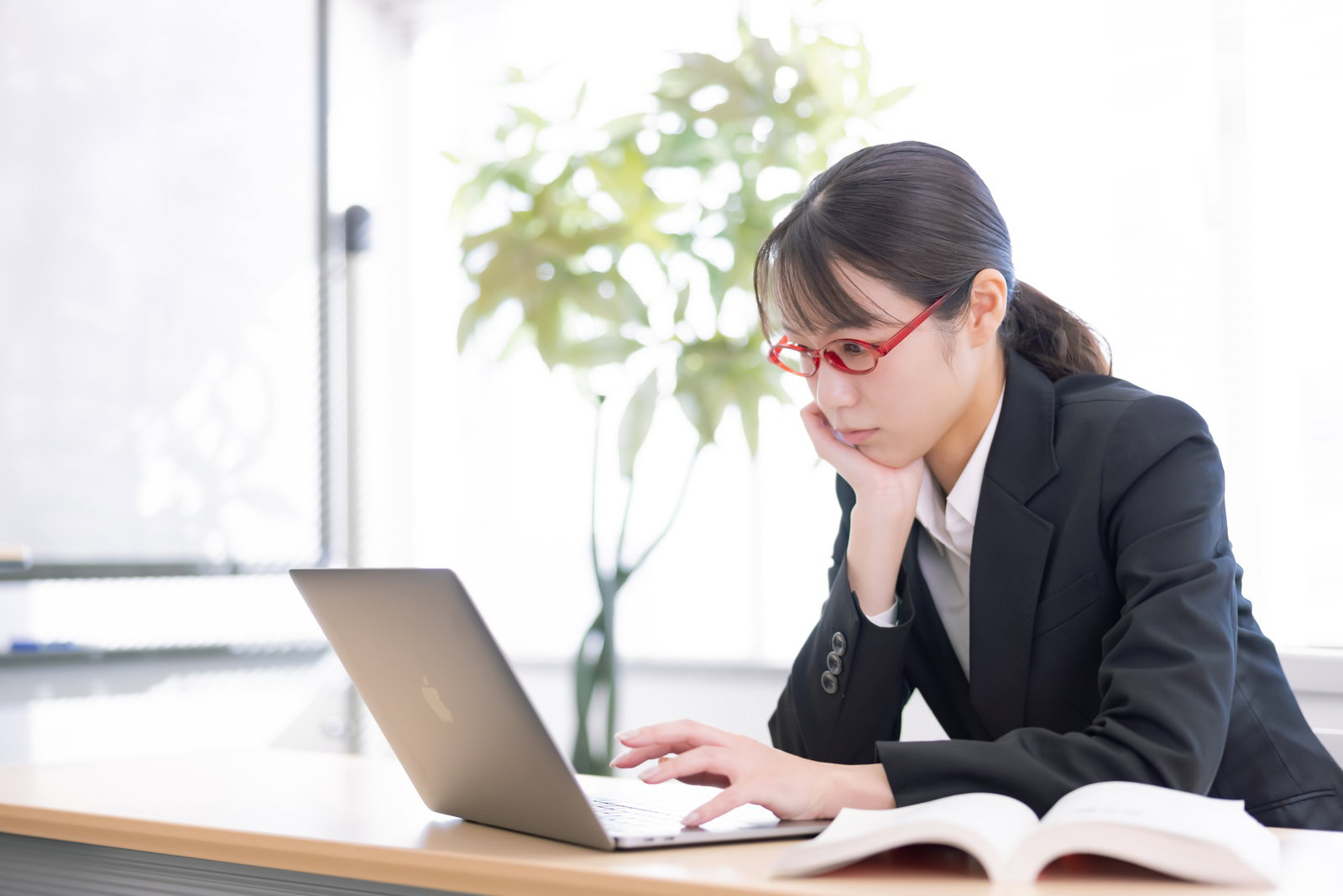 頬杖をつきながらパソコンで検索する女性社員［モデル：SAKI］
