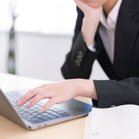 頬杖をつきながらパソコンのキーボードに手を添える女性の写真