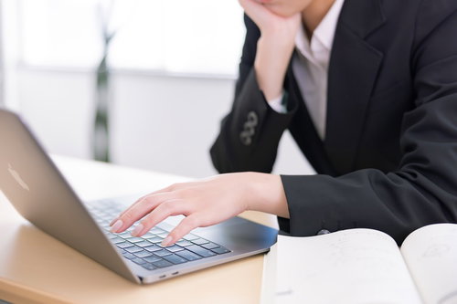 頬杖をつきながらパソコンのキーボードに手を添える女性