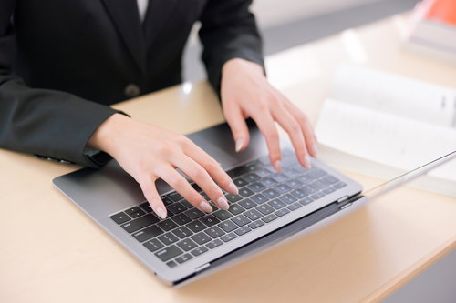 ノートパソコンのキーボードでタイピング中の女性の手元