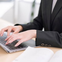 スーツ姿でノートパソコンのキーボードをタイピングする手元の写真