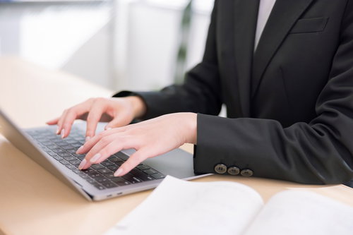スーツ姿でノートパソコンのキーボードをタイピングする手元