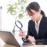 拡大鏡を使ってノートパソコンの画面をチェックする女性社員の写真