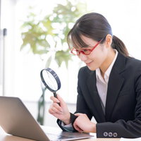 虫眼鏡を覗いてほくそ笑む女性会社員の検索風景の写真