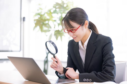虫眼鏡を覗いてほくそ笑む女性会社員の検索風景