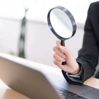 ノートパソコンに向けて虫眼鏡で調べる女性の写真