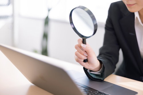 ノートパソコンに向けて虫眼鏡で調べる女性