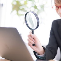 虫メガネを通してディスプレイを確認する眼鏡をかけた女性の写真