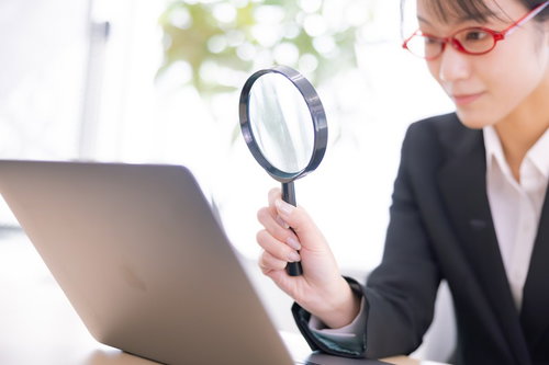 虫メガネを通してディスプレイを確認する眼鏡をかけた女性