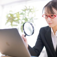 虫眼鏡とノートパソコンを持つ女性社員がデータチェックの写真