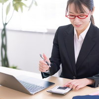 赤い眼鏡をかけた電卓を使う女性事務員の経理業務の写真