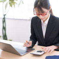 電卓で経費の計算をするメガネ女子の写真