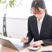 赤いメガネをかけて電卓で計算する会社員女性の写真