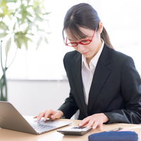 赤いメガネをかけた女性社員が電卓で計算に集中の写真