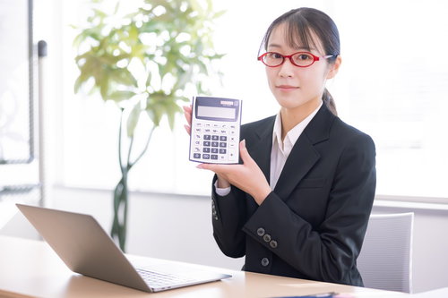 電卓を持って説明する赤いメガネの会社員女性