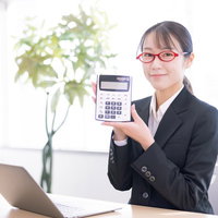 赤いメガネをかけた女性会社員が電卓を手に持つオフィスの写真