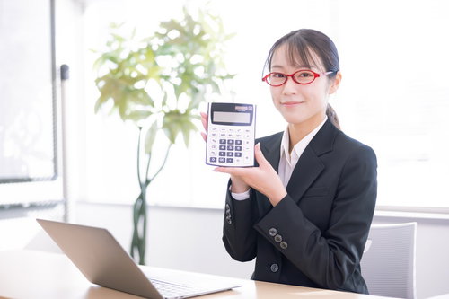 赤いメガネをかけた女性会社員が電卓を手に持つオフィス