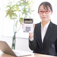 白い電卓を手に持つ赤いメガネの女性会社員の写真