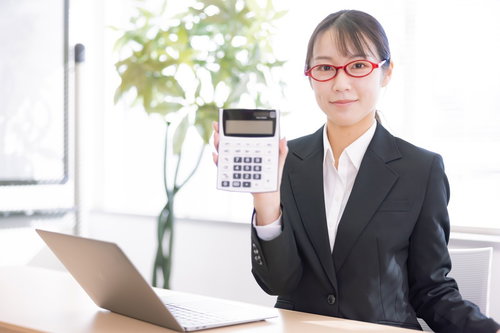 白い電卓を手に持つ赤いメガネの女性会社員