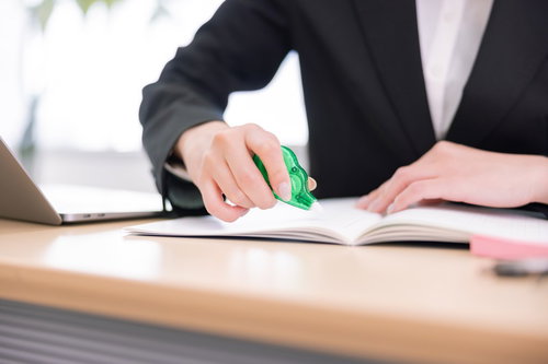 修正テープを持つ事務所女性の手元、書類訂正作業